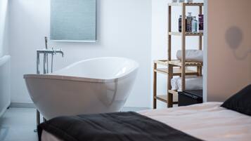 Un baño moderno con una bañera independiente, un estante de madera con artículos de aseo y un ventanal grande.