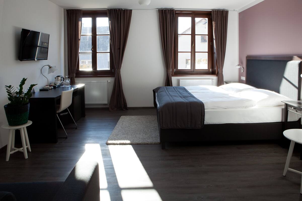 A modern hotel room with a bed, desk, chair, and a TV mounted on the wall.