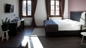 A modern hotel room with a bed, desk, chair, and a TV mounted on the wall.