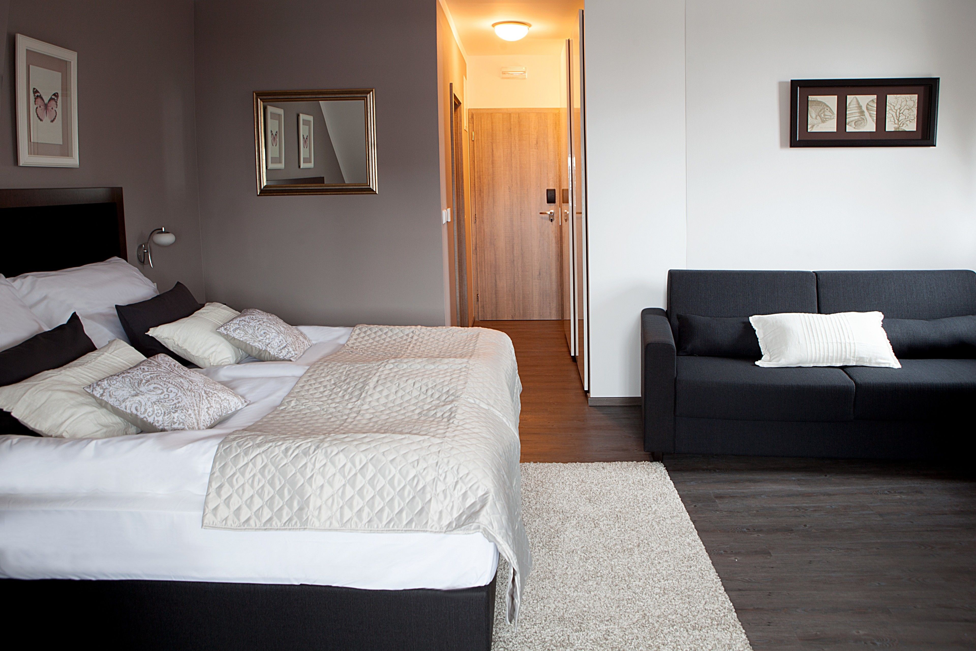 Ein Schlafzimmer mit einem Bett, einem dunklen Sofa, einer Holztür und gerahmten Kunstwerken an den Wänden.
