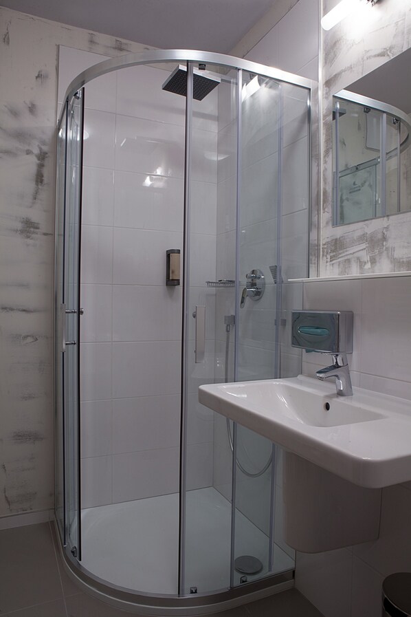 Un baño moderno con ducha de vidrio, lavamanos blanco y pared con azulejos de mármol.