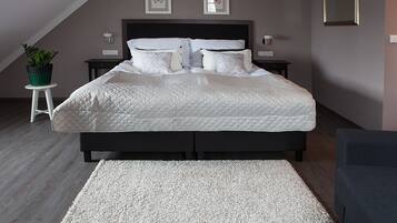 A neatly made bed with a quilted duvet, a white rug, and a small potted plant on a white stool.