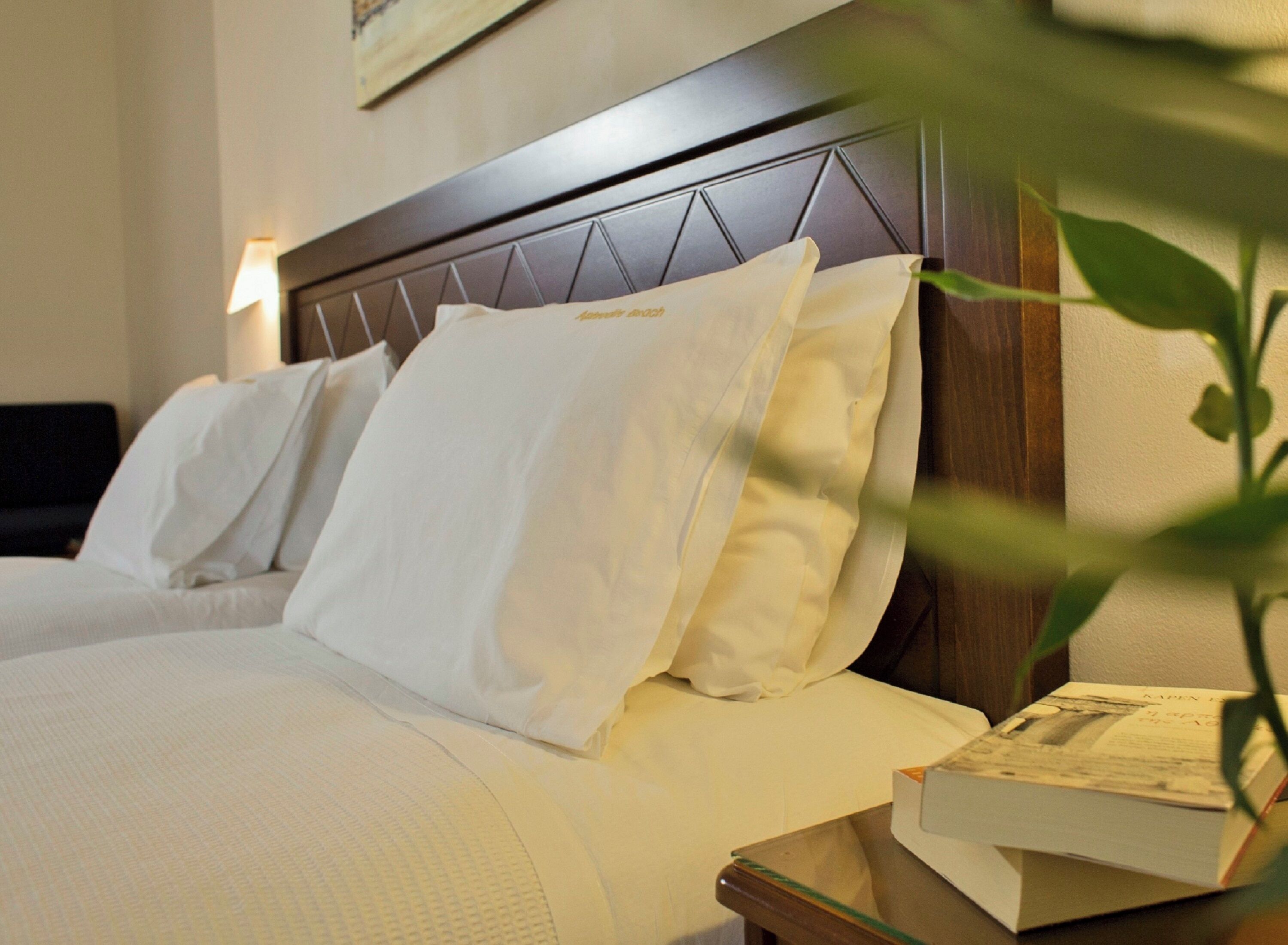 A hotel room with a neatly made bed, a wooden headboard, and a bedside table with a book.
