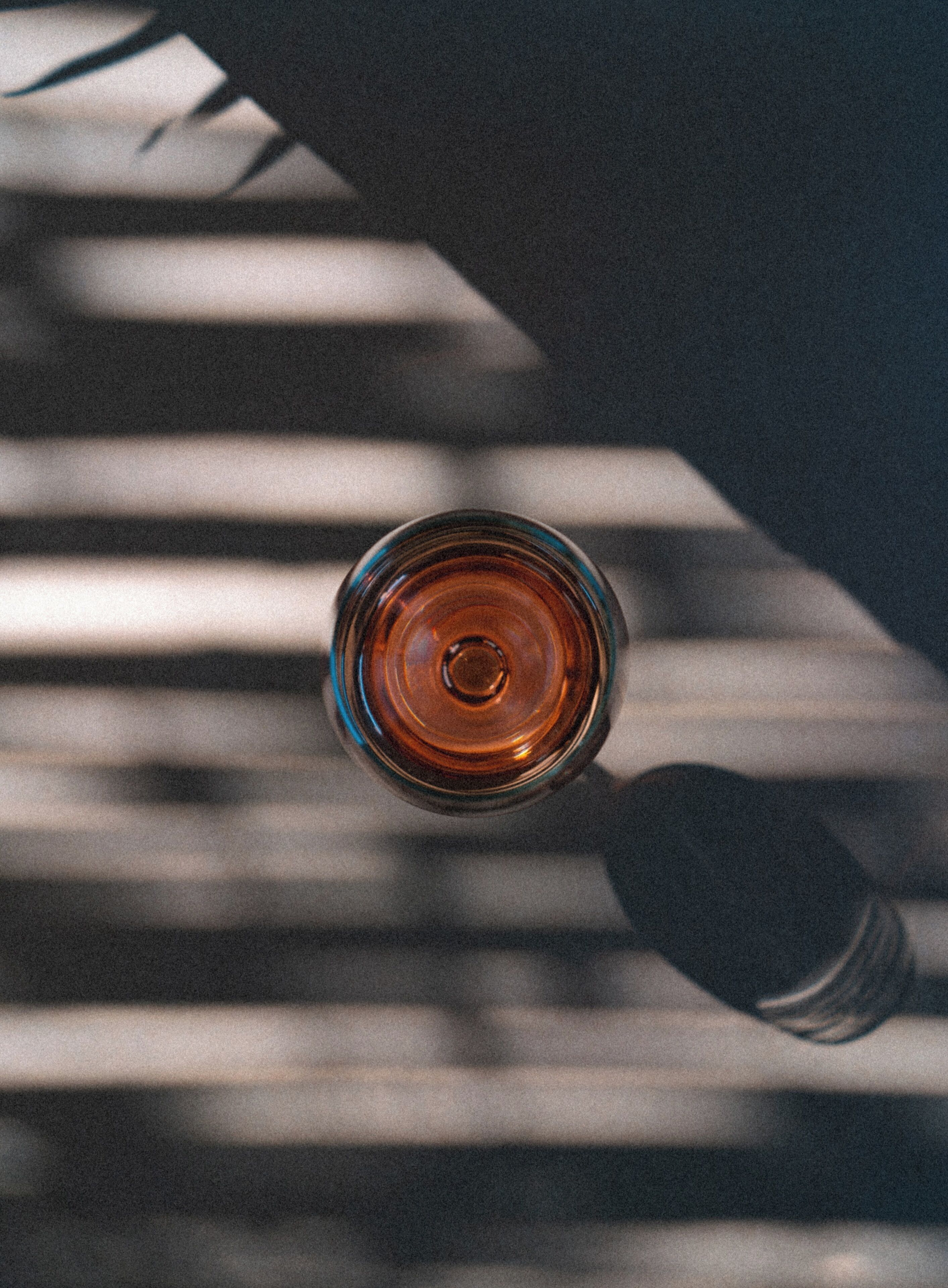 Vista cenital de un vaso con un líquido marrón, probablemente una bebida, sobre una superficie con sombras a rayas.