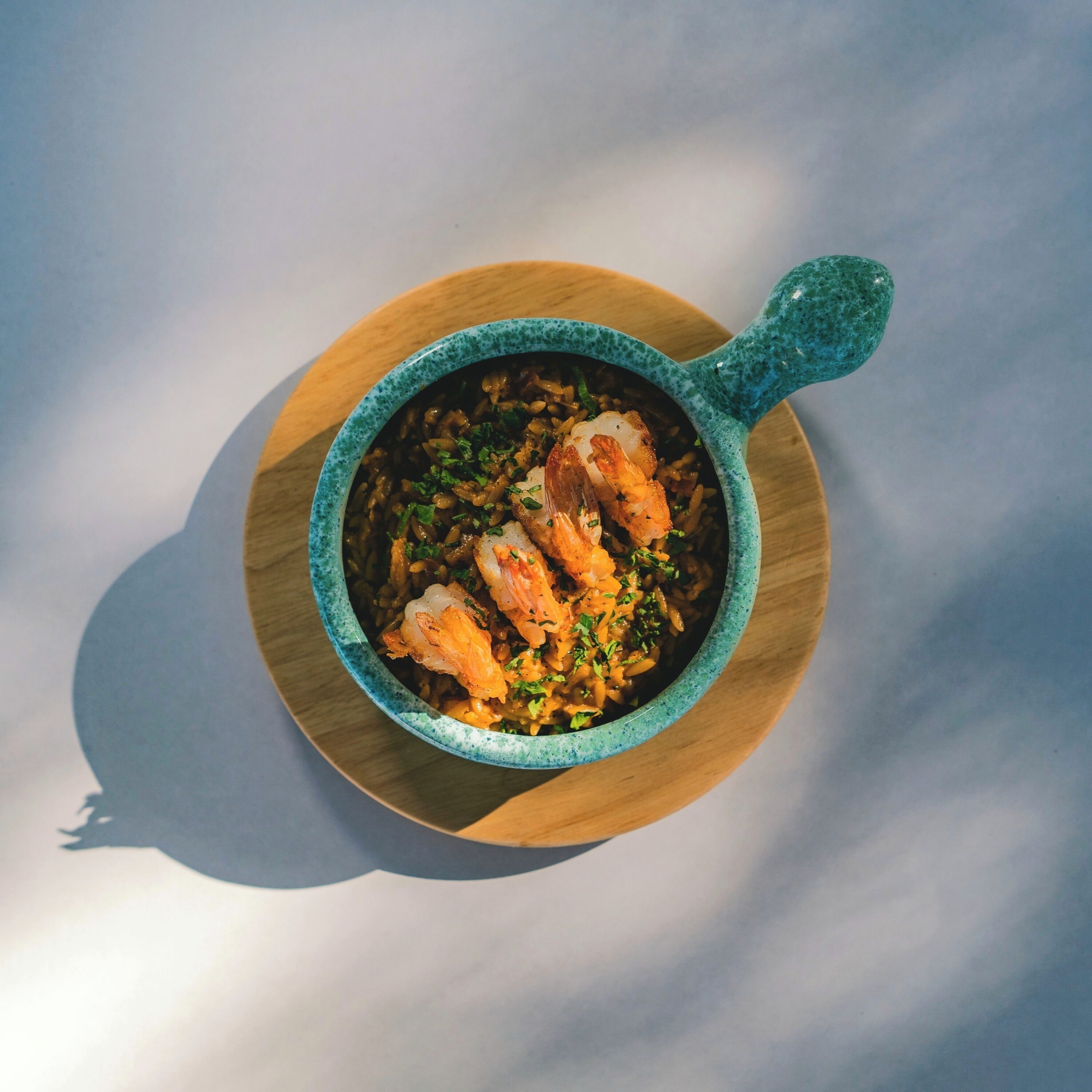 A bowl of food with shrimp on a wooden board.