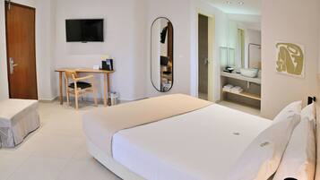 A hotel room with a bed, a desk, a chair, a TV, a mirror, and a bathroom visible through an open door.