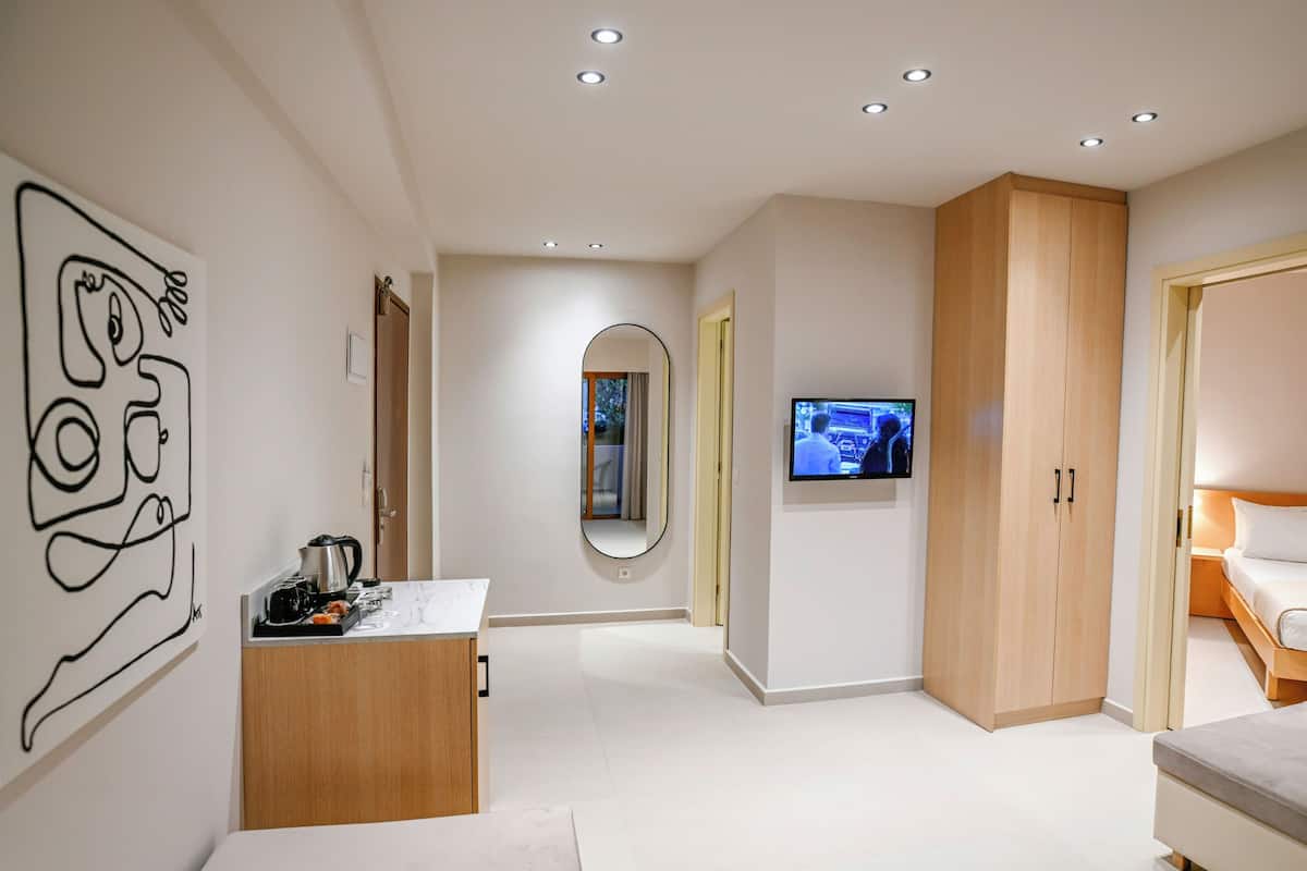 A modern hotel room with a minimalist design, featuring a large mirror, a flat-screen TV, and a wooden wardrobe.