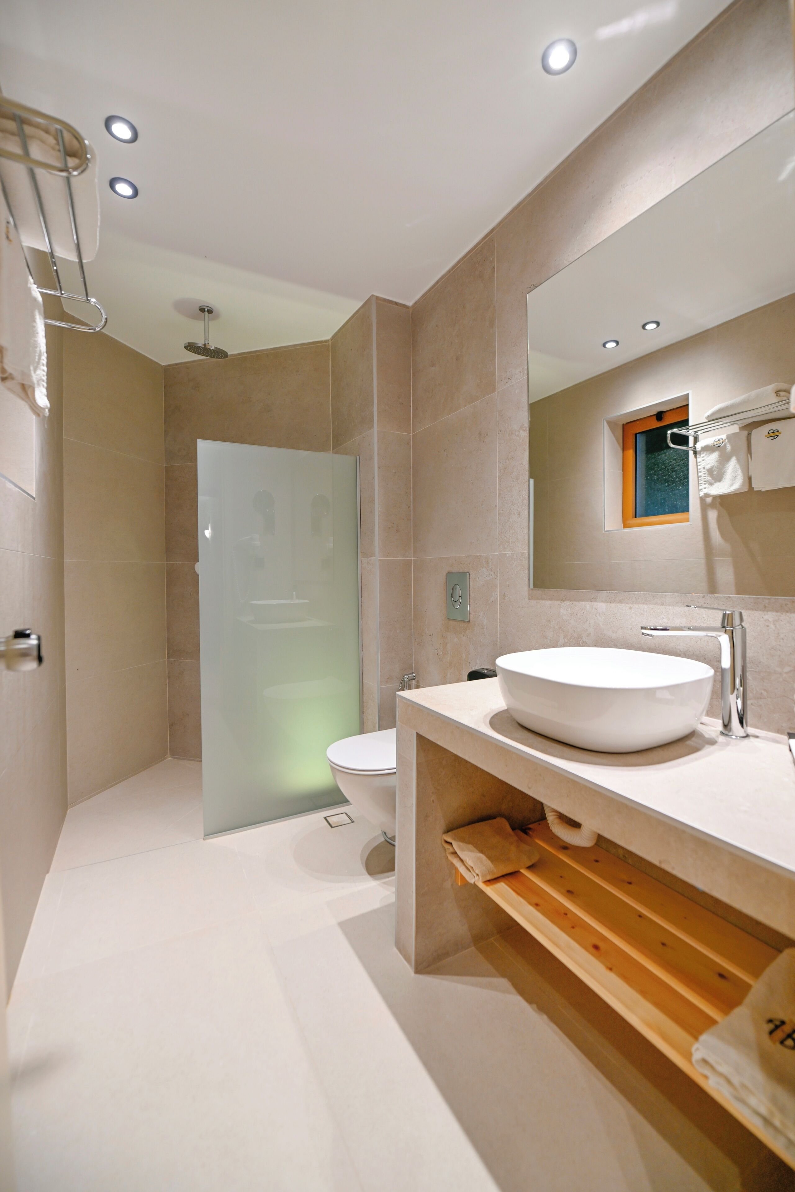 Un baño moderno con un lavabo grande de color blanco, cabina de ducha con paredes de vidrio y repisa de madera debajo del lavabo.