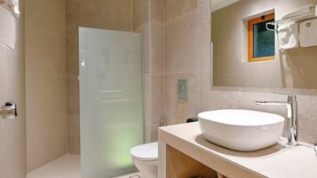 Un baño moderno con un lavabo grande de color blanco, cabina de ducha con paredes de vidrio y repisa de madera debajo del lavabo.