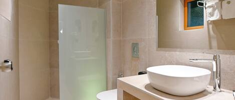 Un baño moderno con un lavabo grande de color blanco, cabina de ducha con paredes de vidrio y repisa de madera debajo del lavabo.