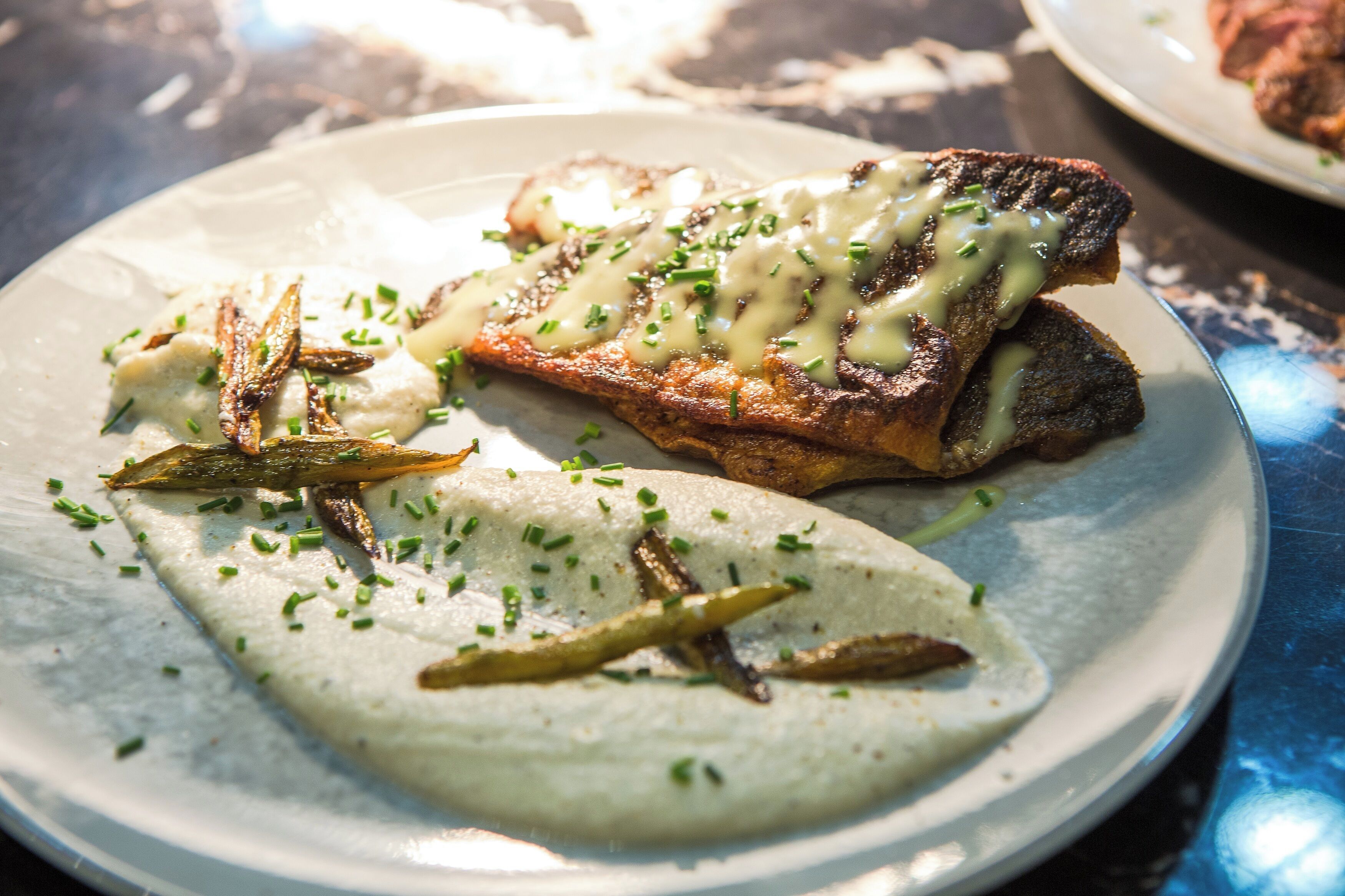 A plate with grilled meat, a creamy sauce, and garnished with chives.