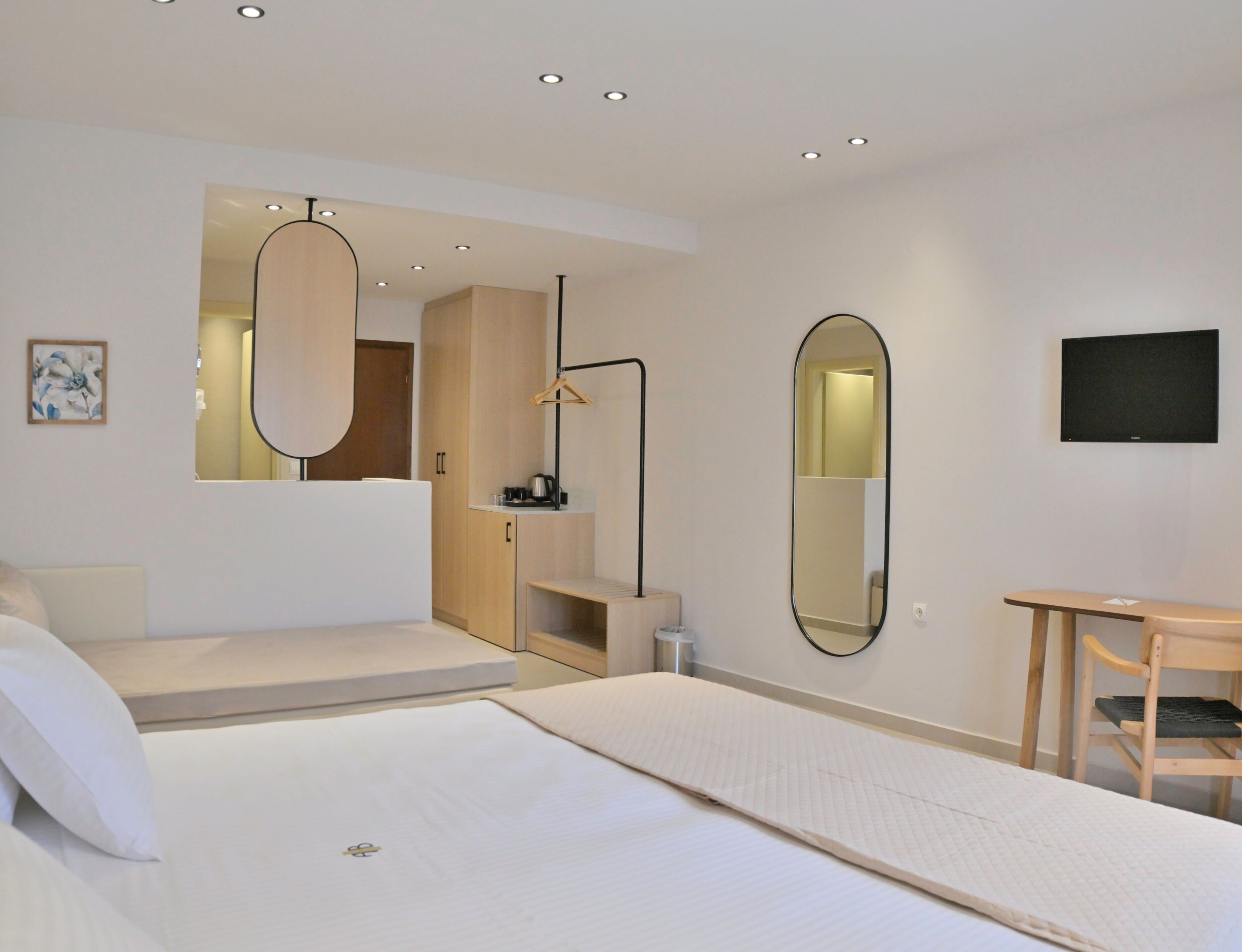 A modern hotel room with a bed, a desk, a mirror, and a television.