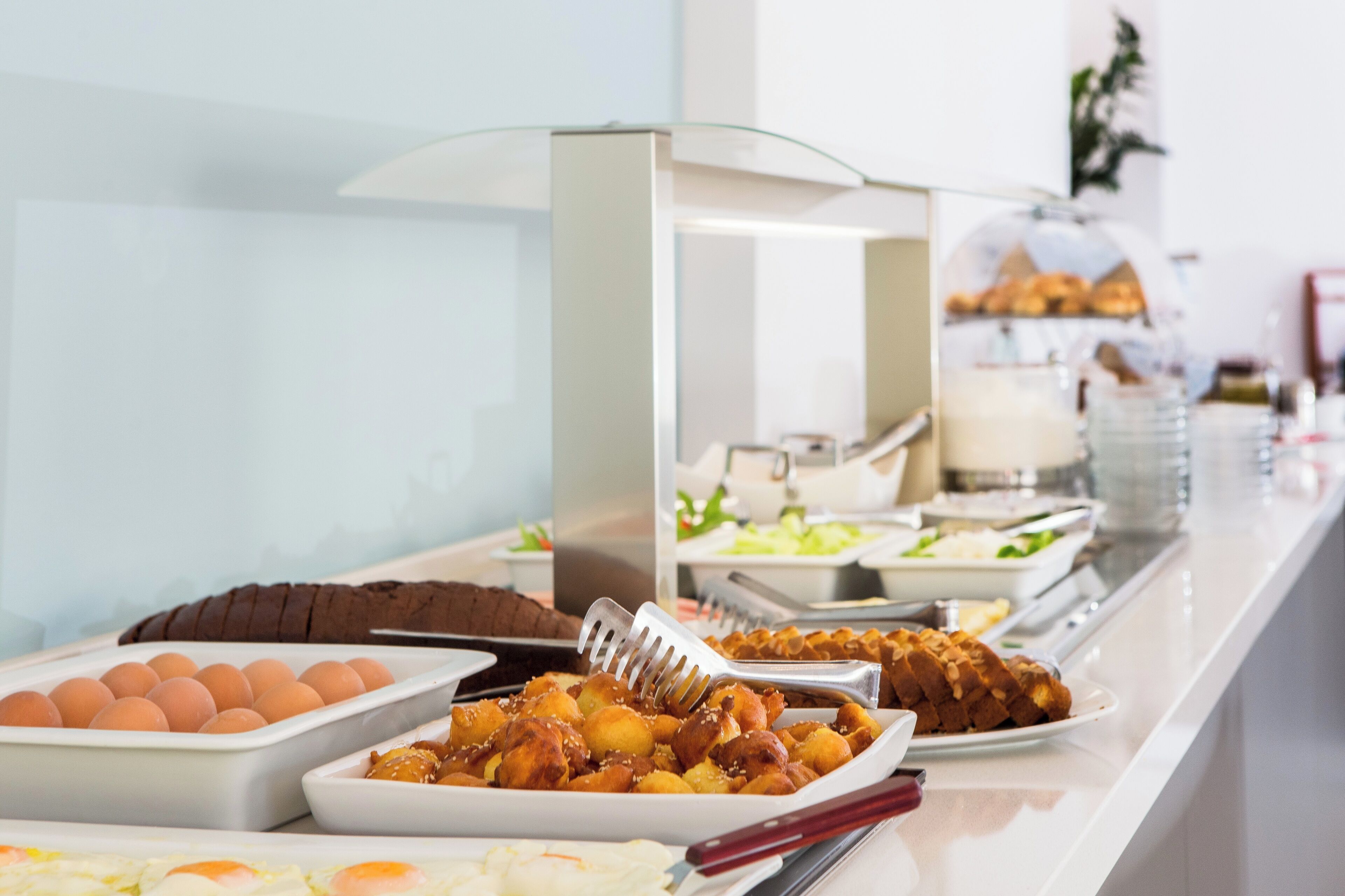 Un buffet proposant une variété de plats, notamment des œufs, des viennoiseries et un plat pané.