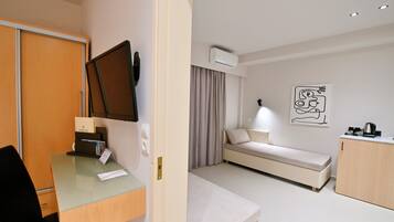 A modern hotel room with a desk, a bed, a small sofa, a coffee machine, and a painting on the wall.