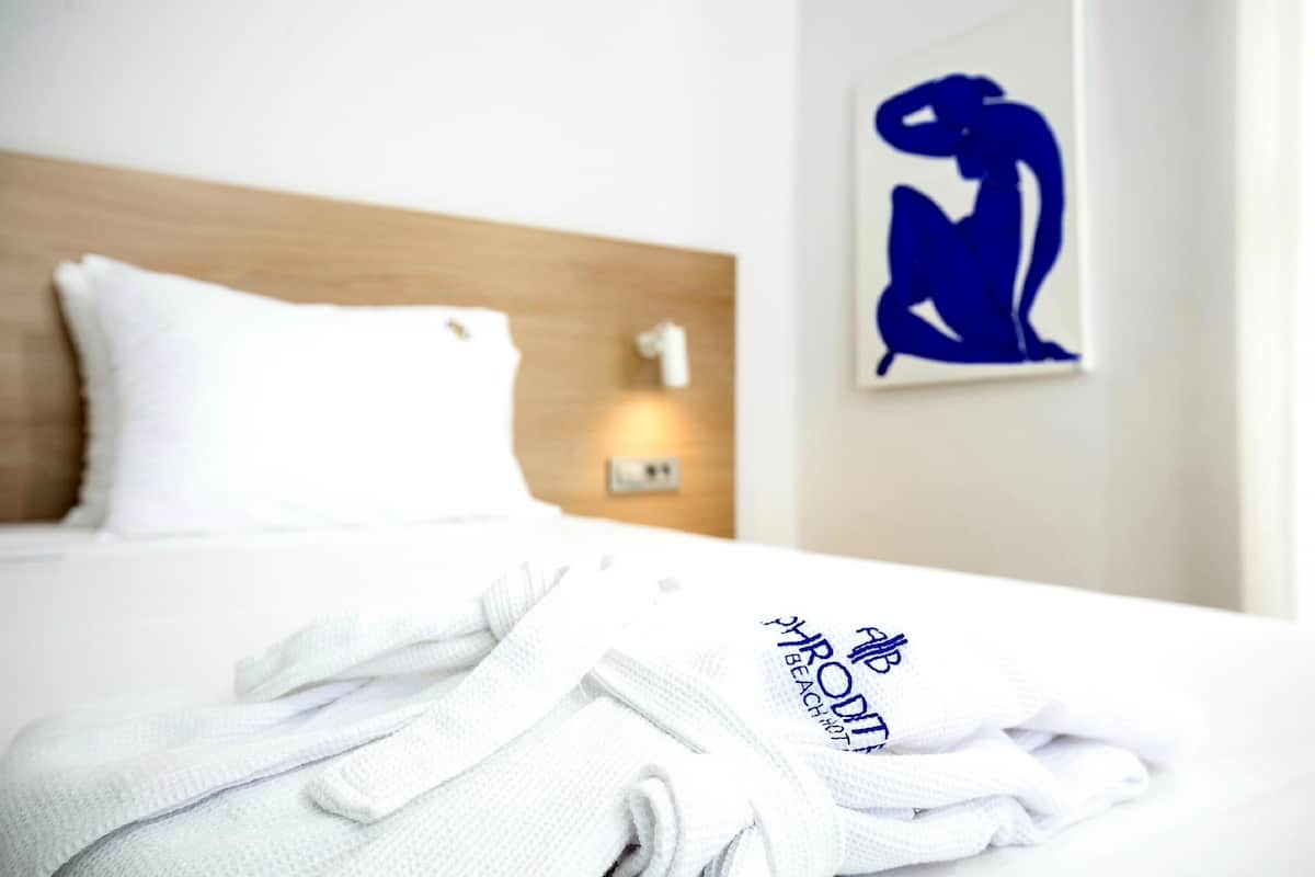 A neatly made bed with white bedding and a folded white robe on it.