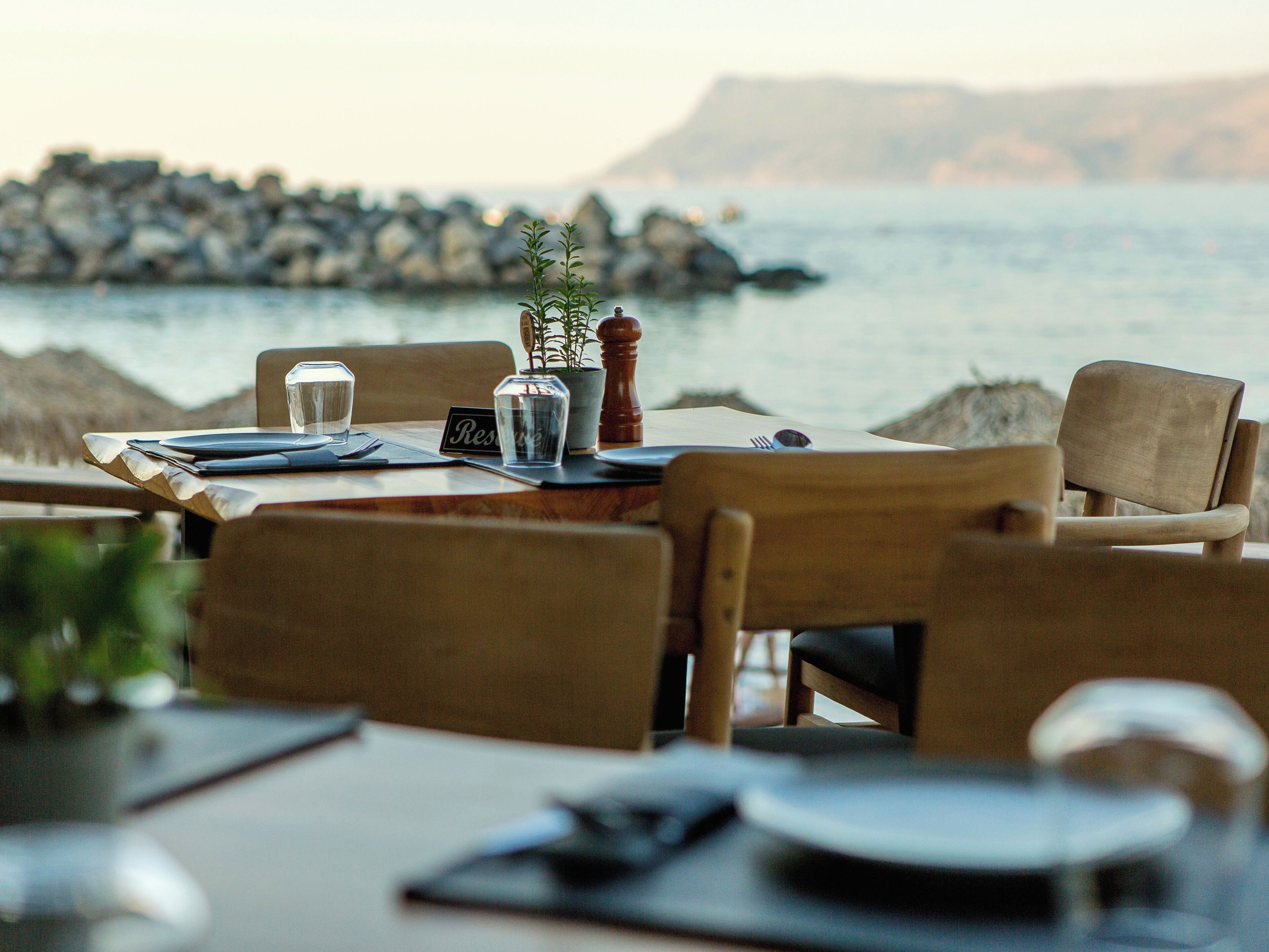 A table set for two with a view of the sea and rocks in the background.