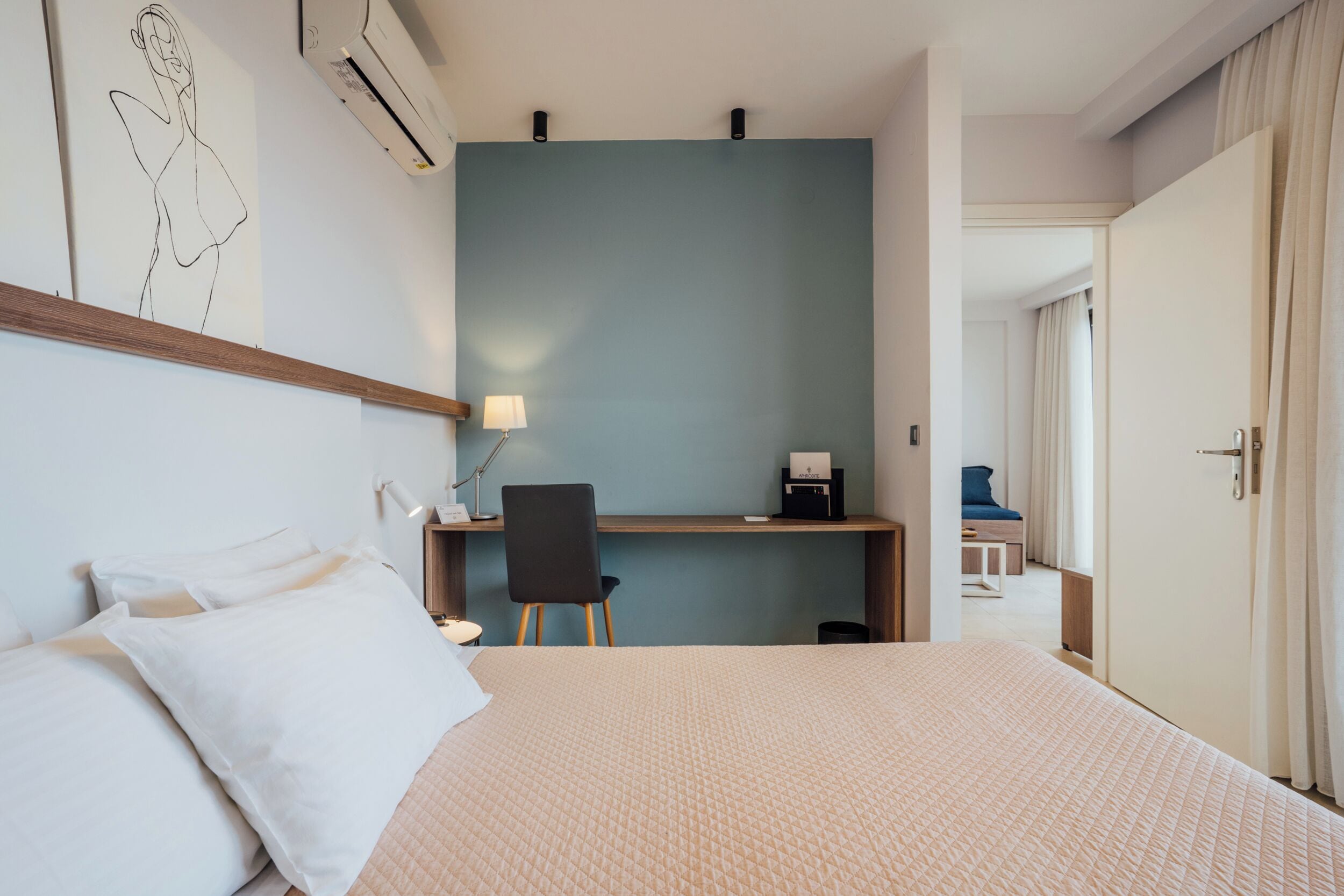 A hotel room with a bed, a desk, a chair, and a door.