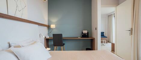 A hotel room with a bed, a desk, a chair, and a door.