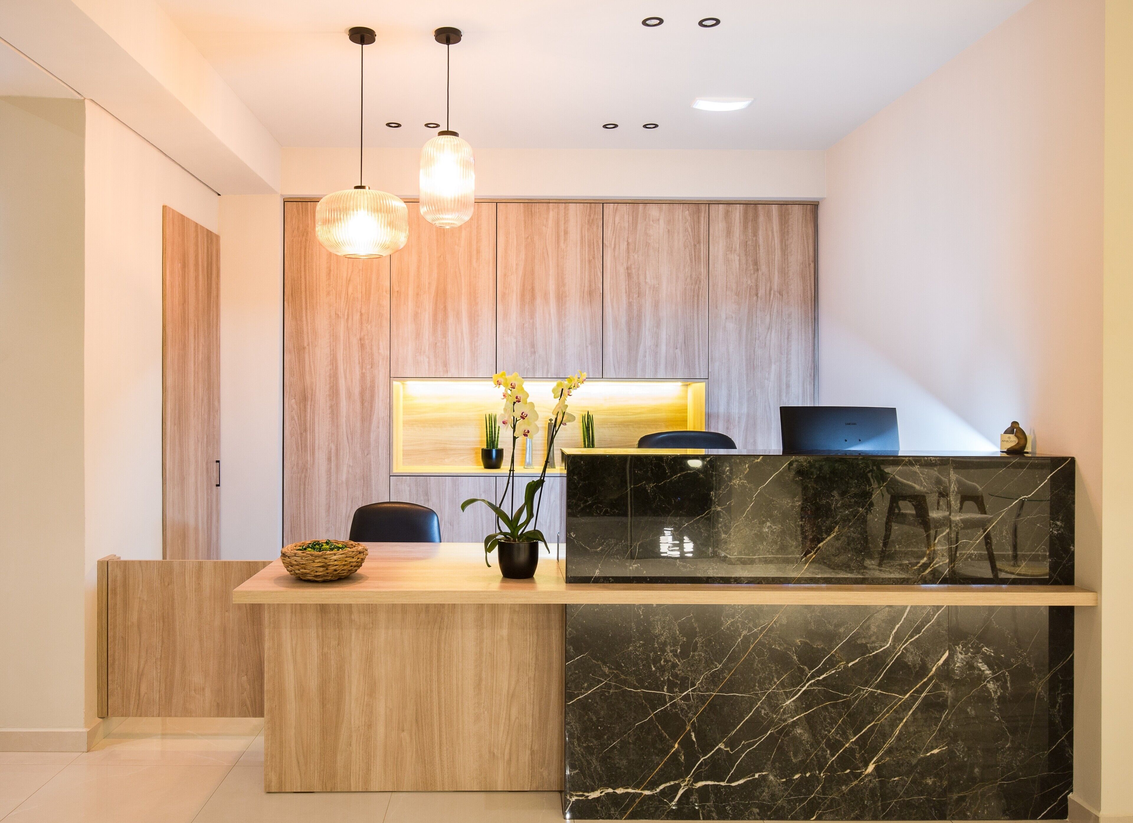 A modern reception desk with a marble top, wooden panel backdrop, and pendant lighting.