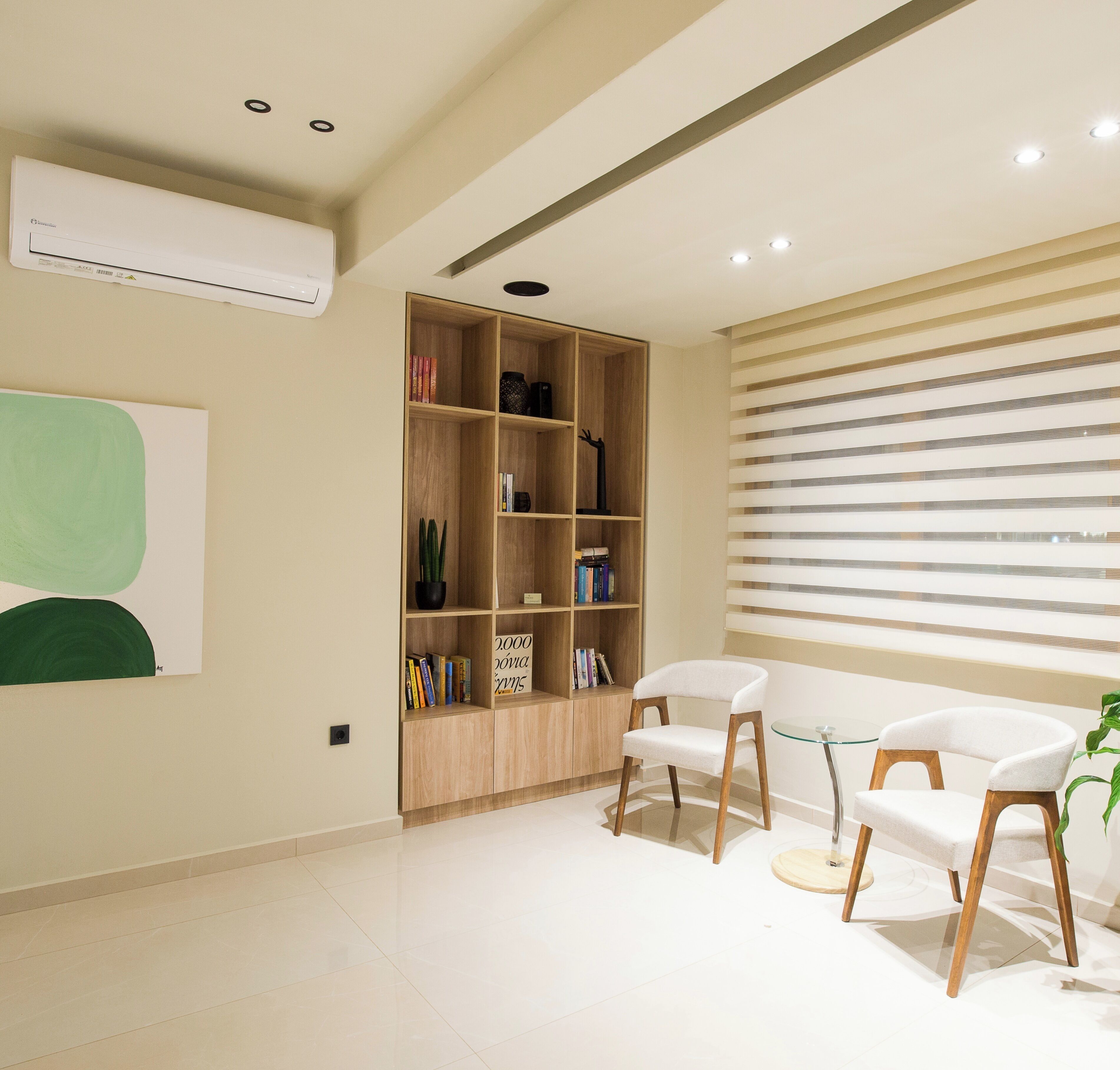A modern living room with a wooden bookshelf, two white chairs, and a large window with blinds.