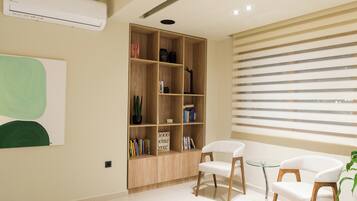Un salón moderno con una estantería de madera, dos sillones blancos y un ventanal con persianas.