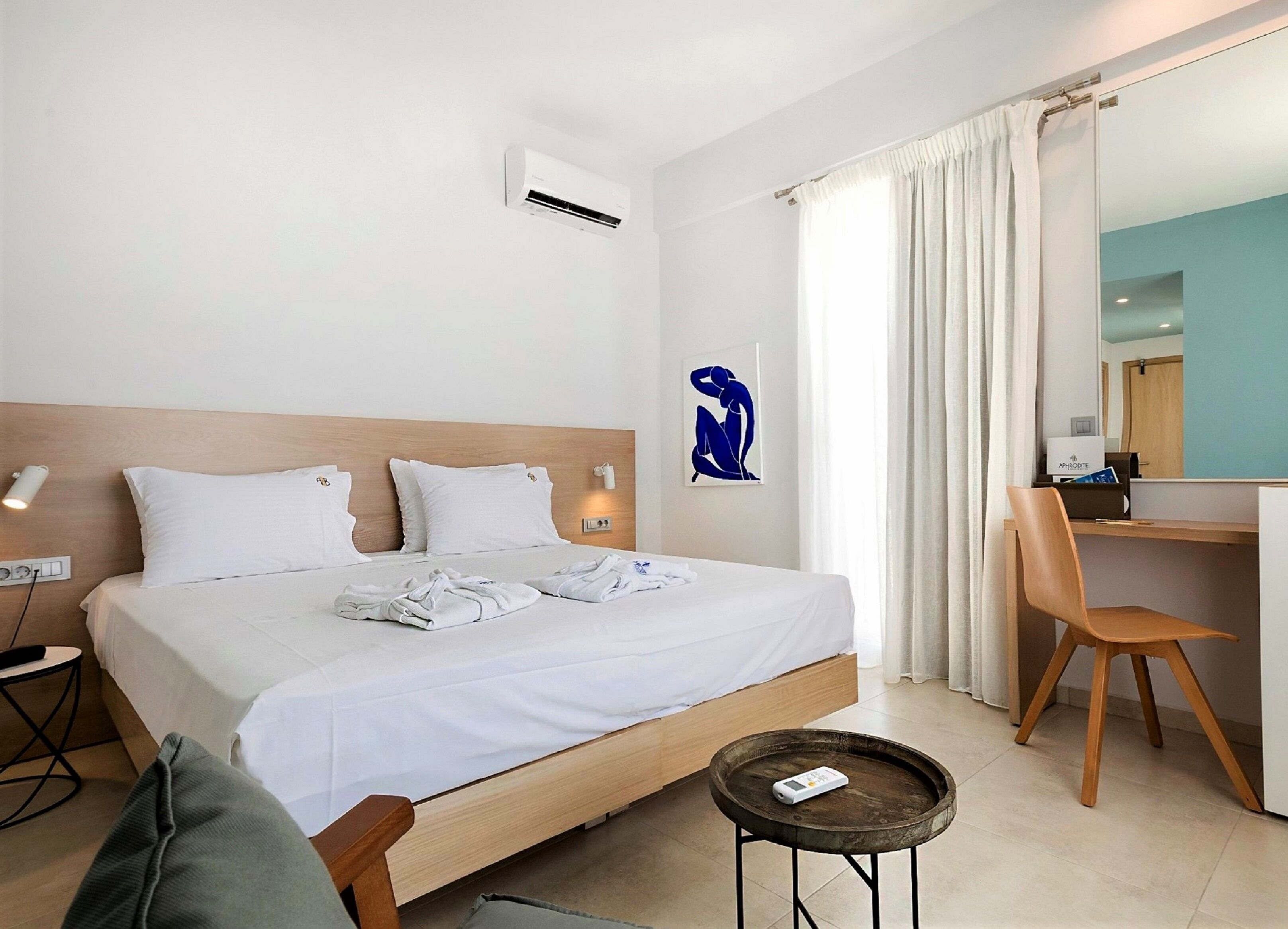 A hotel room with a bed, a desk, a chair, an air conditioner, and a wall-mounted artwork.