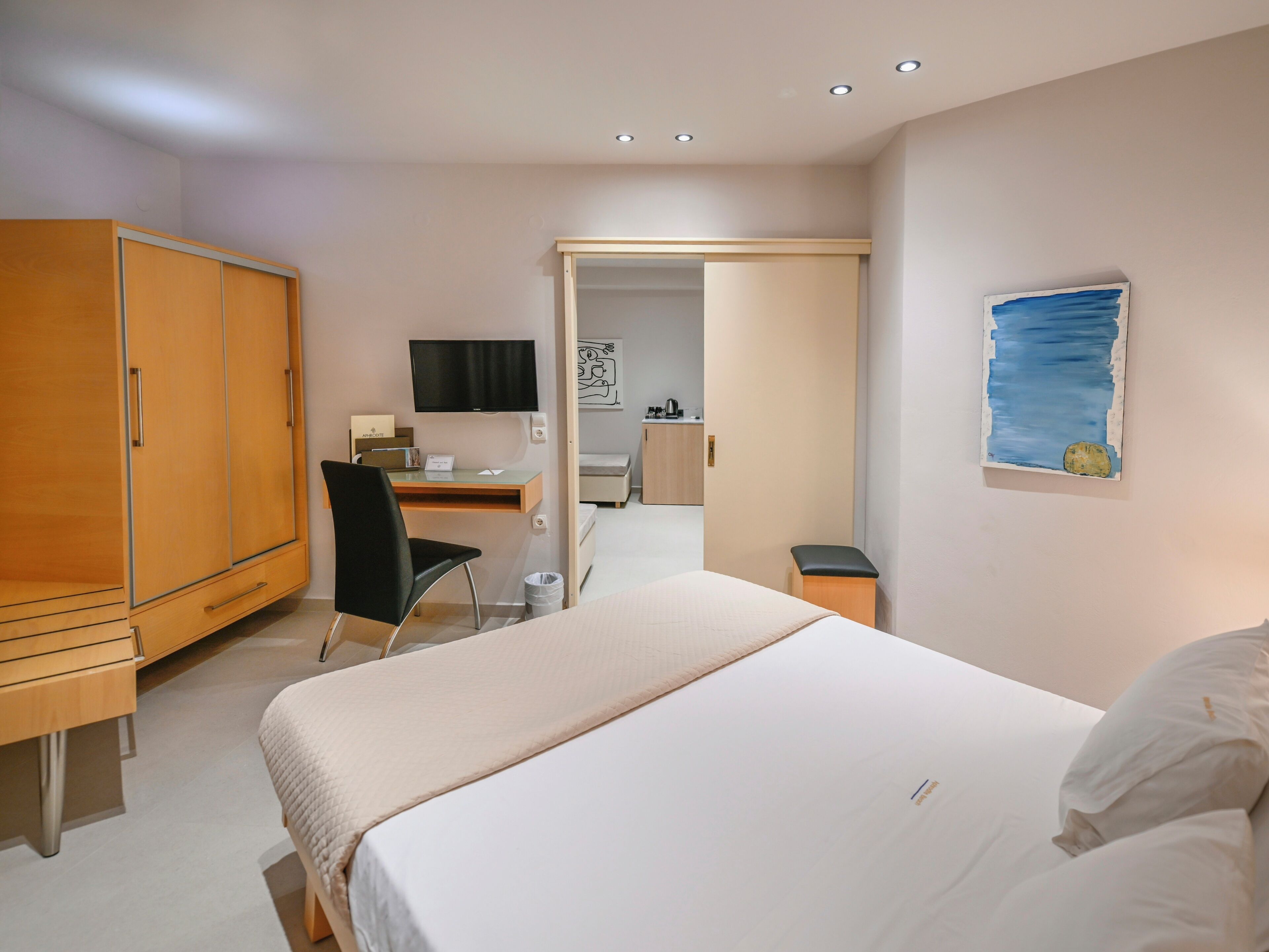 A hotel room with a bed, a desk, a chair, a wardrobe, a television, and a painting on the wall.