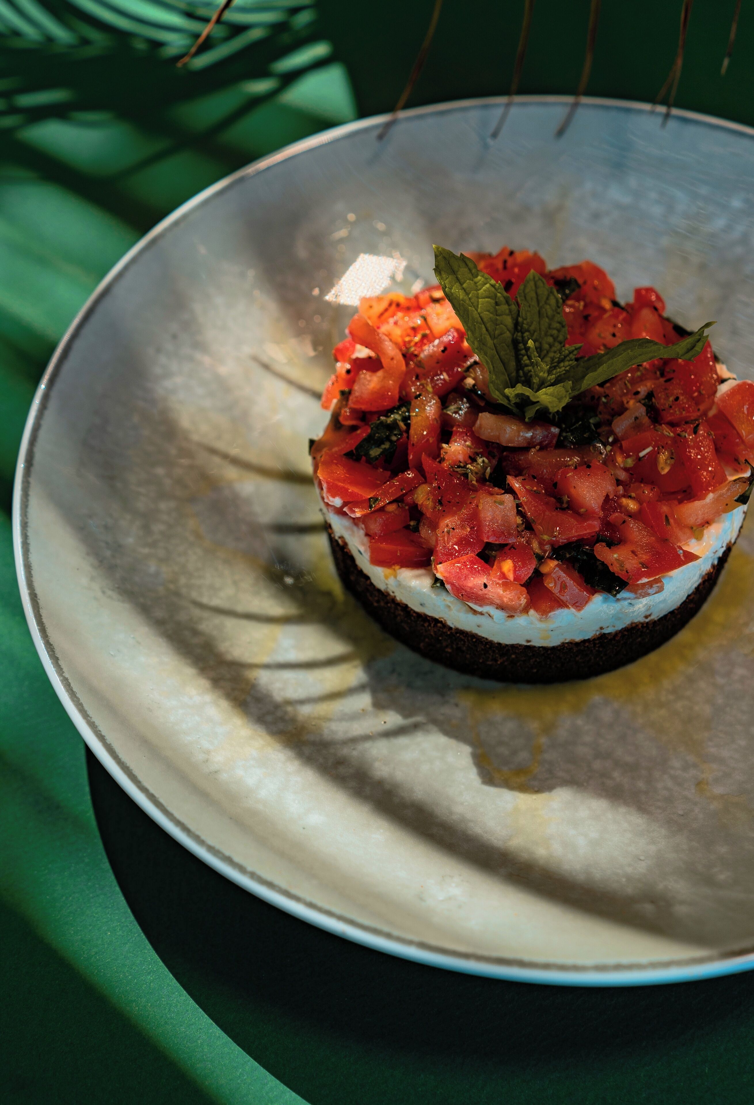 A dish with a white base topped with red ingredients and a green leaf, served on a round plate.