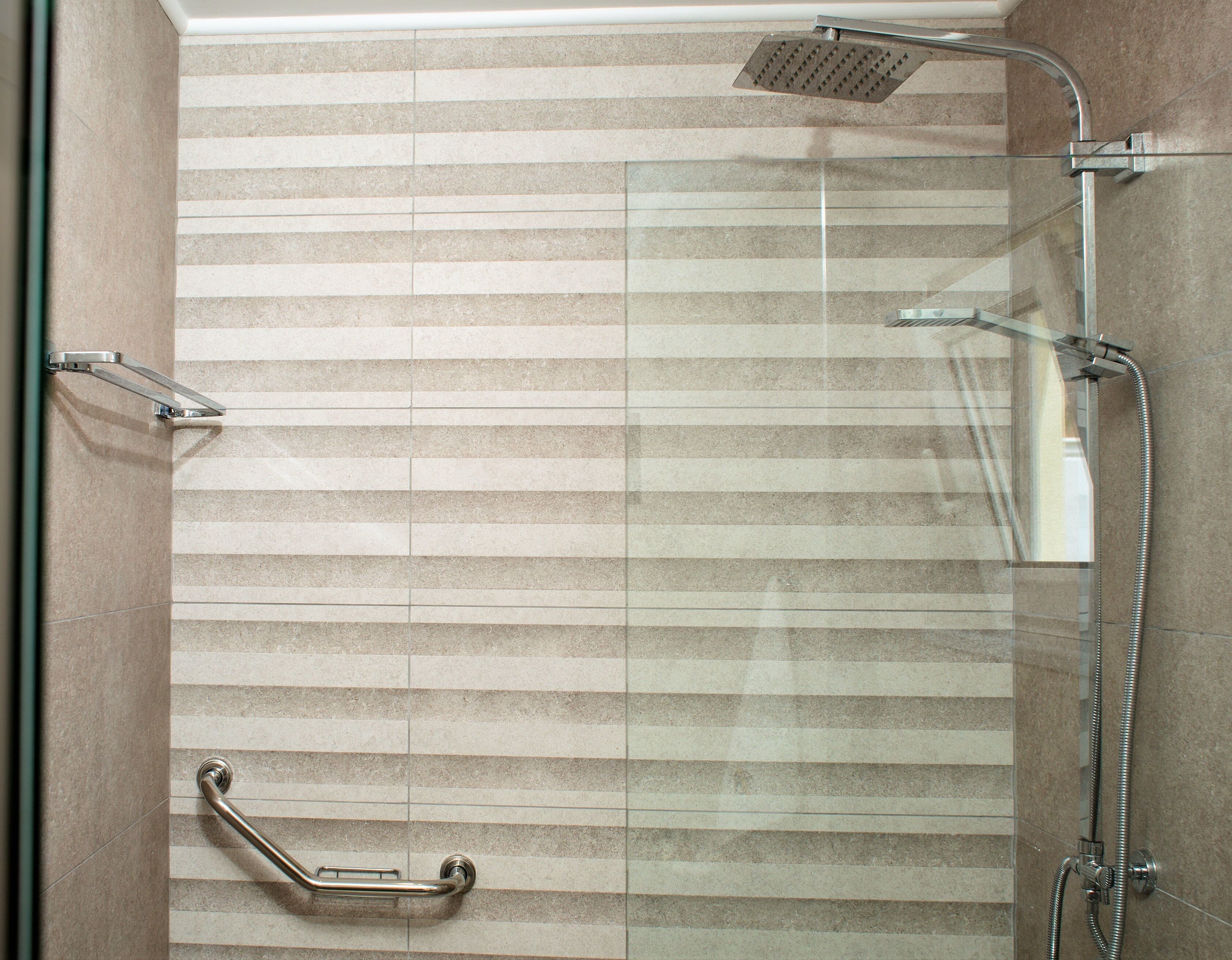 A modern shower area with a glass door, a handheld showerhead, a handheld shower control, and a grab bar for safety.