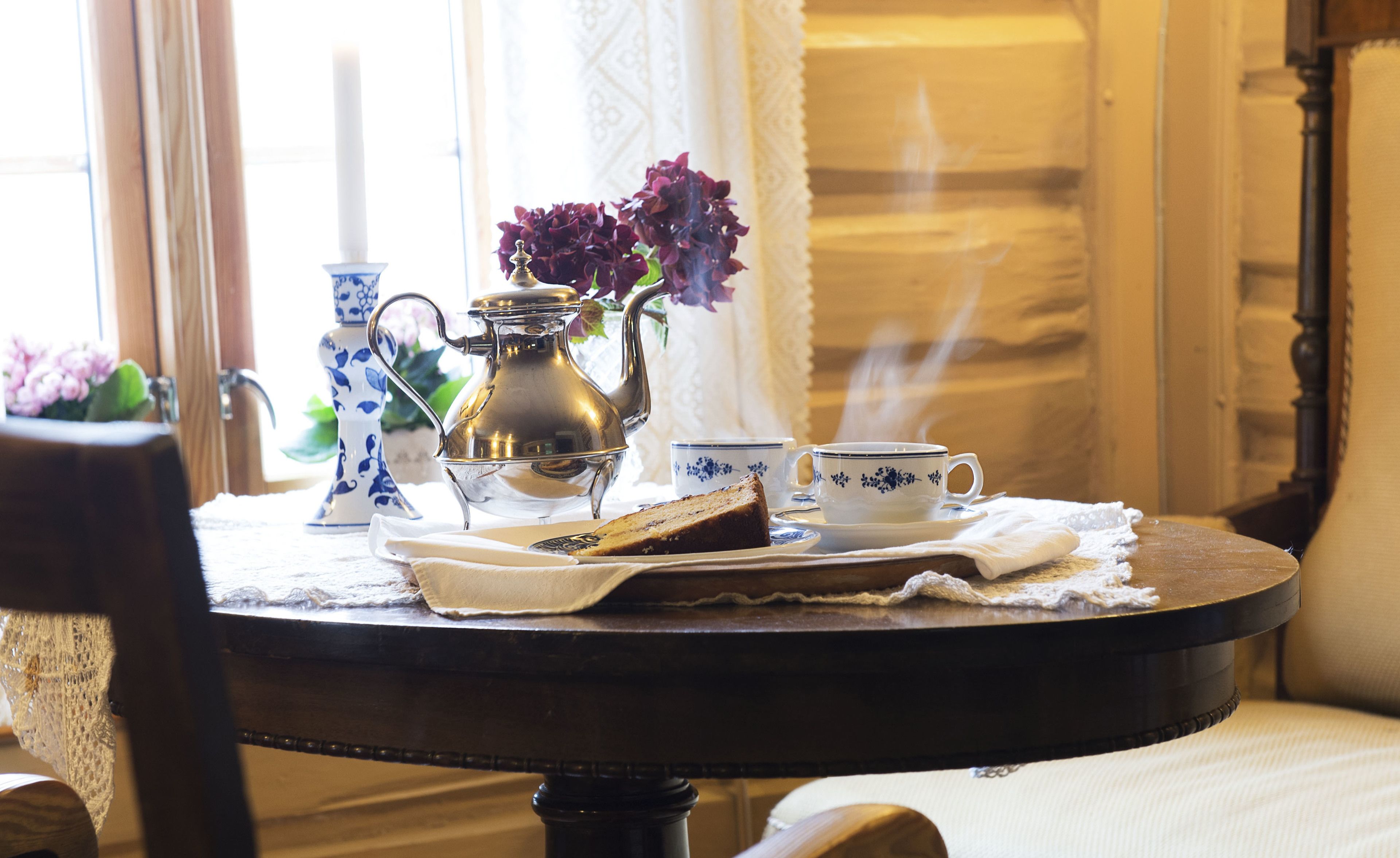 A table with a teapot, a cup, and a slice of cake, set on a lace tablecloth.
