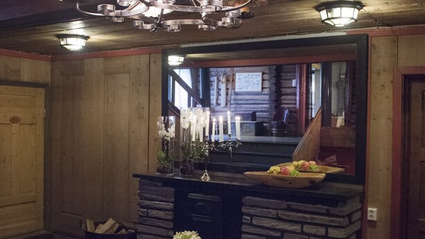 A wooden table with a candle and a vase of flowers, a chandelier, and a stone fireplace. - Glomstad Gjestehus (Øyer)
