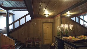 A wooden interior with a stone floor, a wooden door, two chairs, a bar area with fruit, and a staircase. - Glomstad Gjestehus (Øyer)