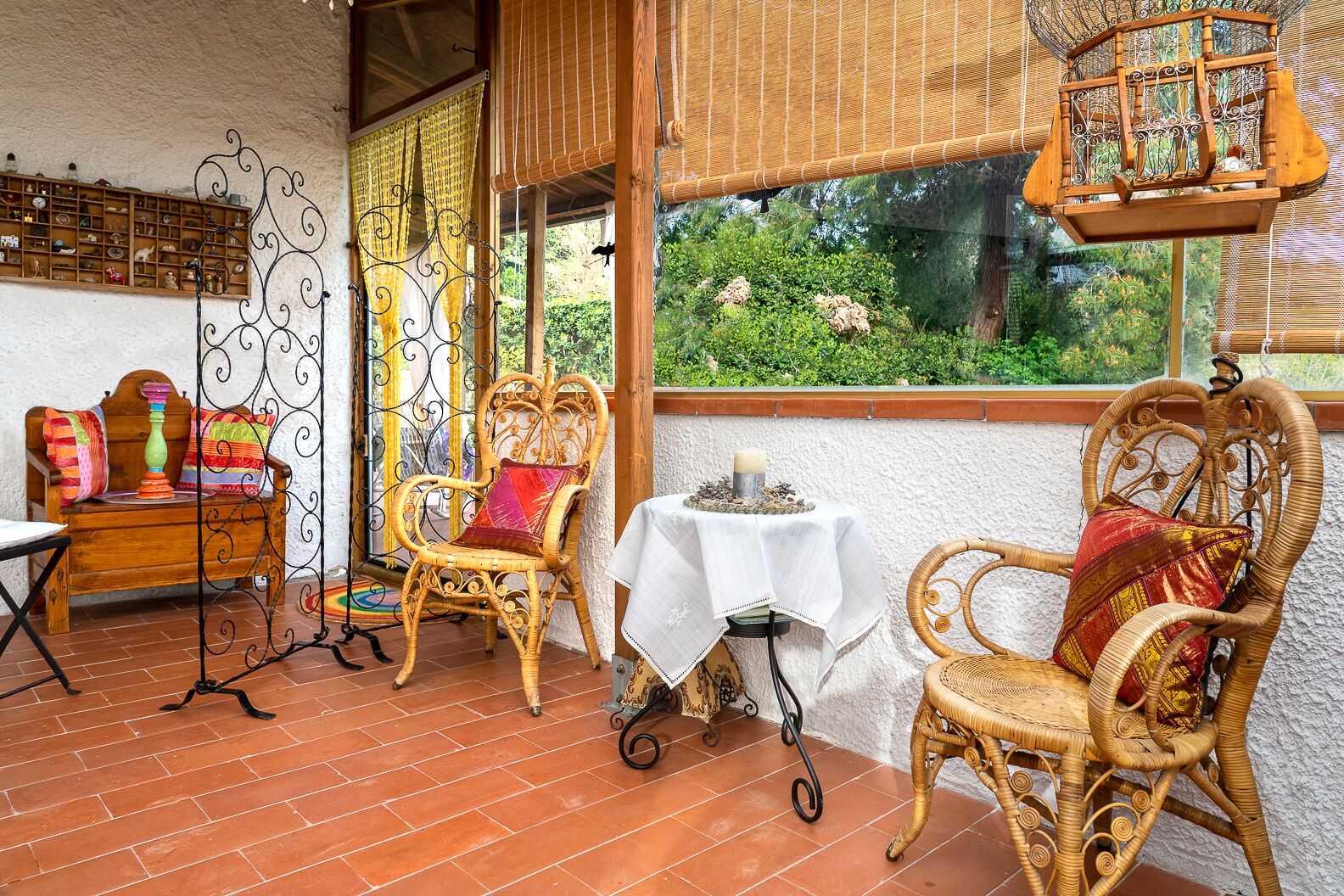 Eine gemütliche Terrasse mit Korbmöbeln, einem kleinen Tisch mit Kerze und Blick ins Grüne.