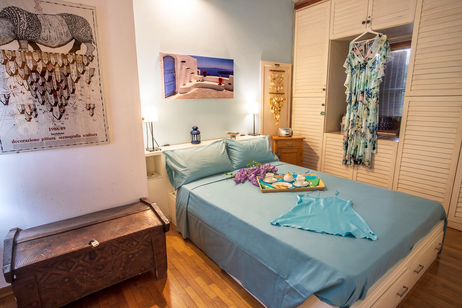 Un dormitorio con cama, cómoda, mesita de noche, lámpara, cuadro y armario.