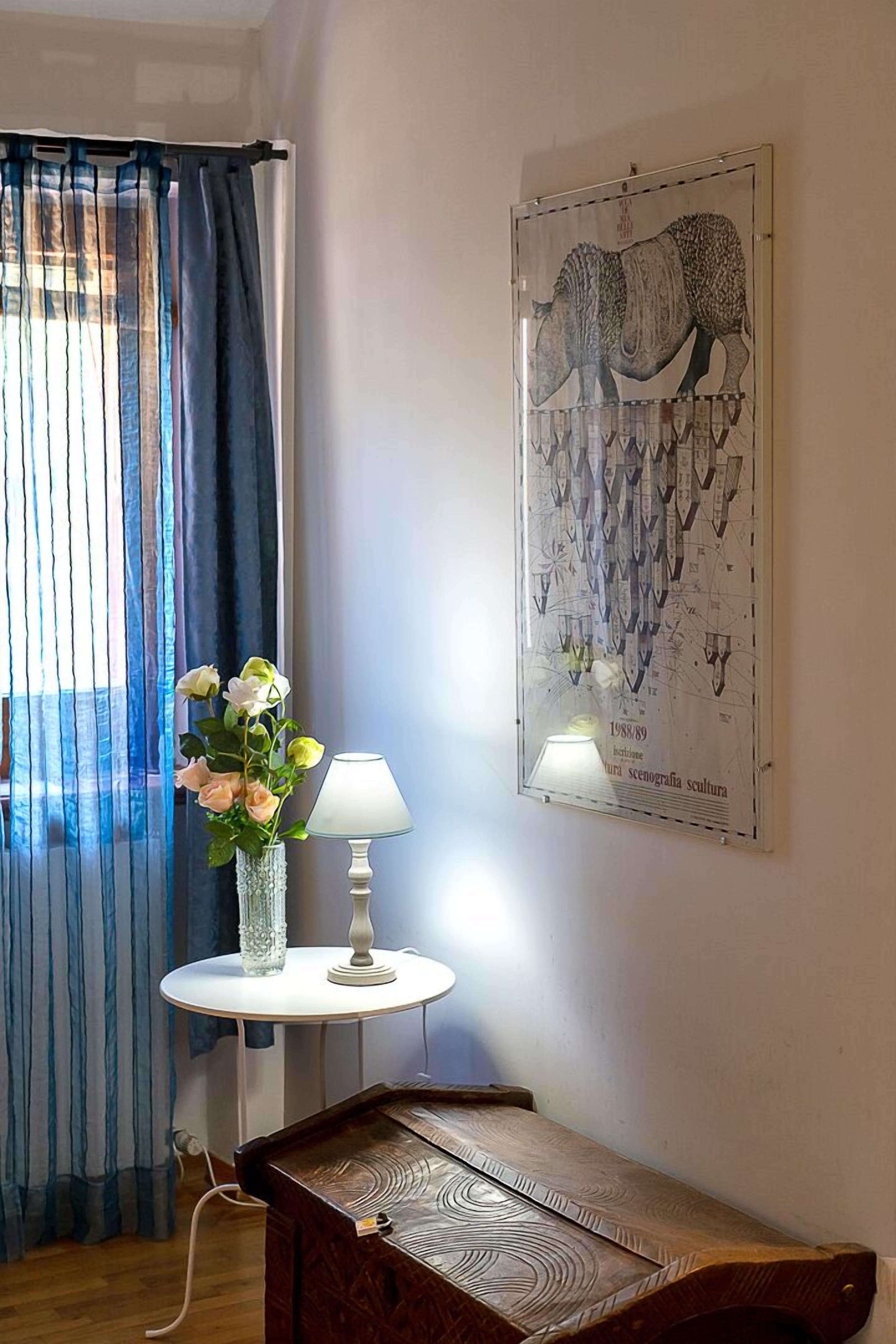 Una habitación con una cama de madera, una mesa blanca con una lámpara, un jarrón con flores y un cartel en la pared.