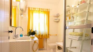 A bathroom with a glass shower enclosure, a white sink with a mirror, yellow curtains, and a yellow rug.