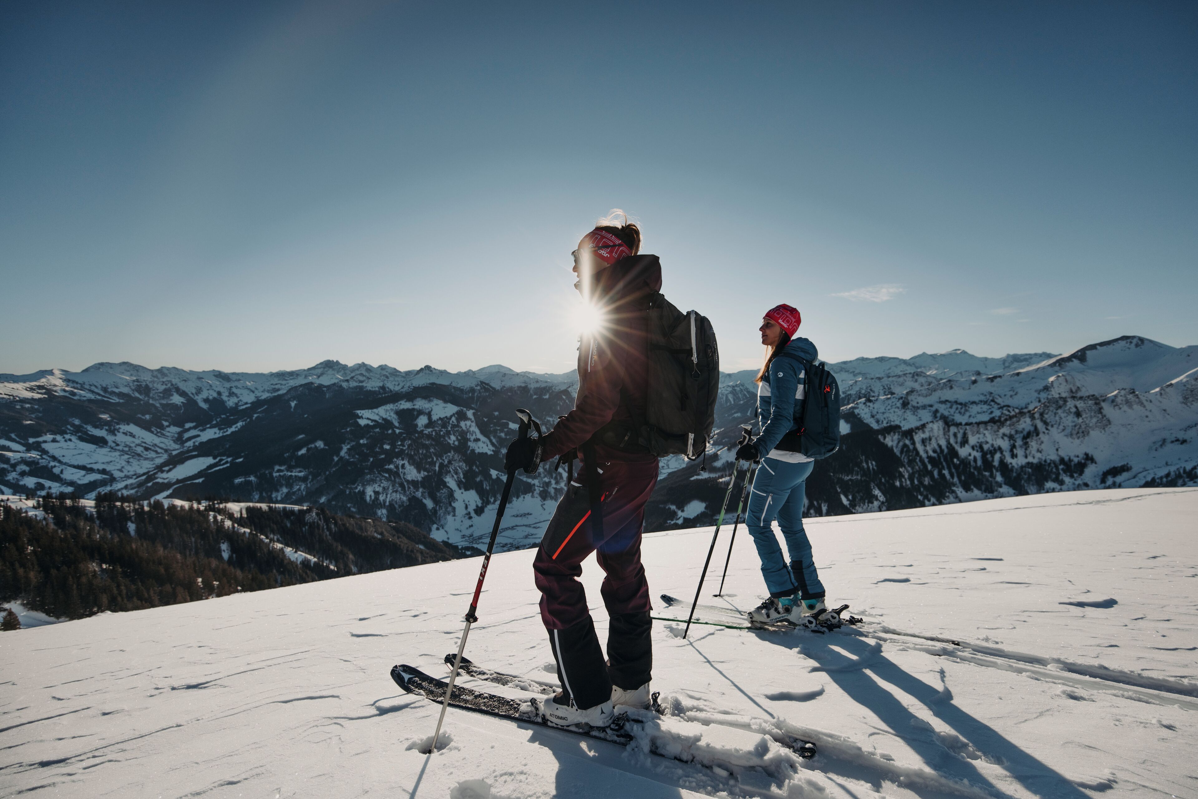 Two skiers on a snowy mountain slope with a clear sky and distant mountains.
