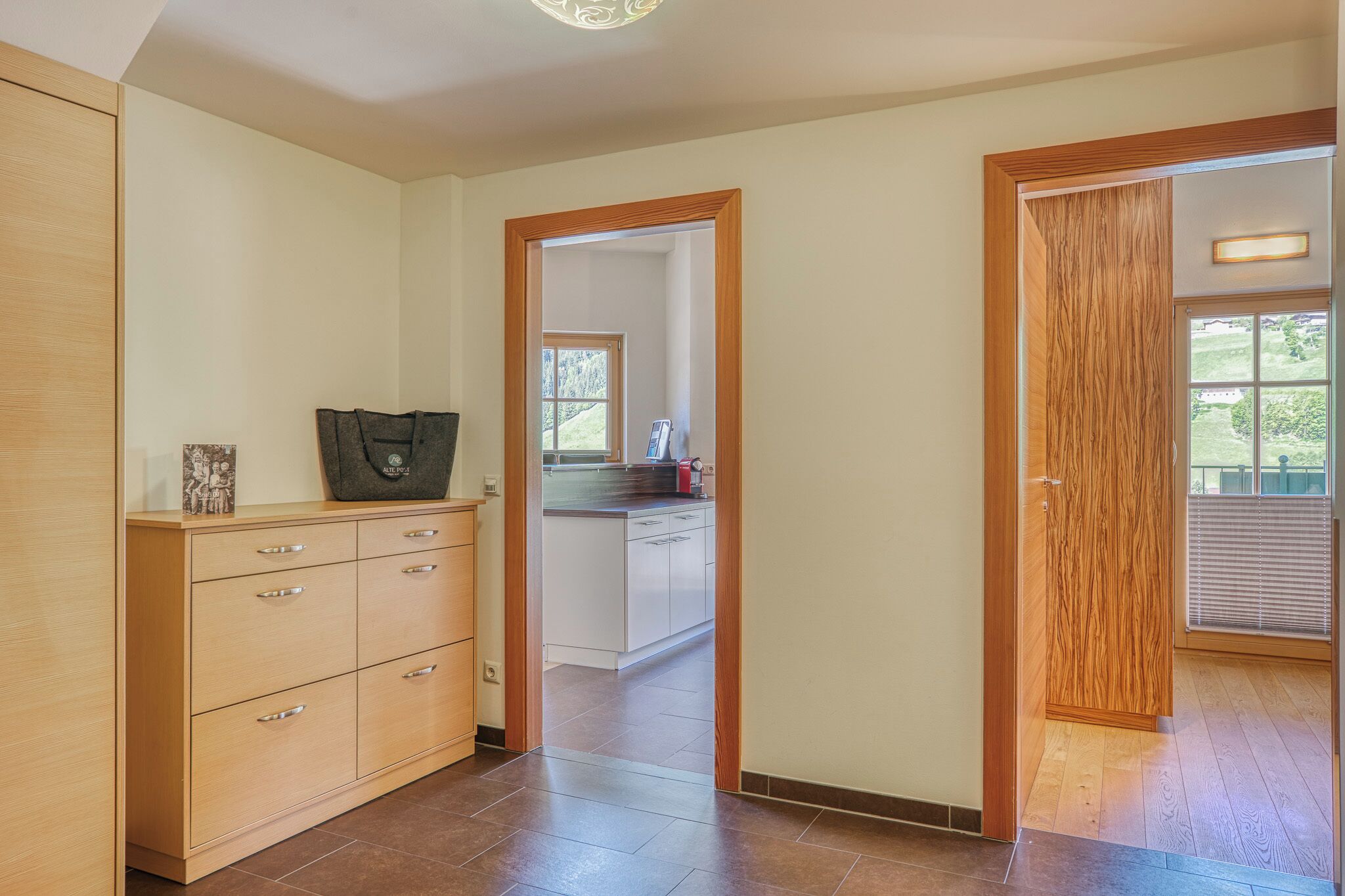 A spacious hallway with a wooden cabinet, a kitchen area with a window, and a door leading to another room.