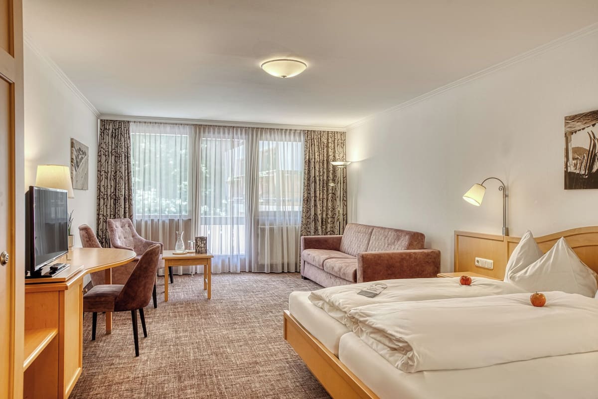 A hotel room with a bed, a desk, a chair, a sofa, and a TV.