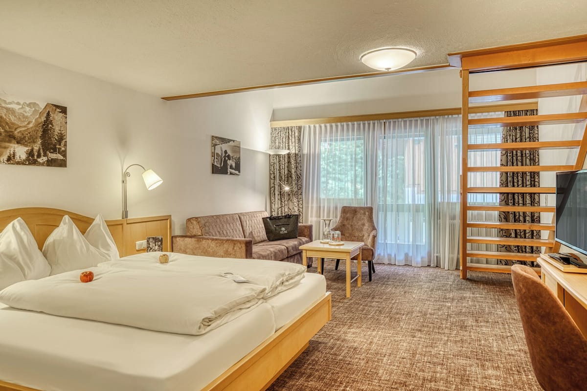 A hotel room with a bed, a sofa, a chair, a small table, a TV, and a window with curtains.