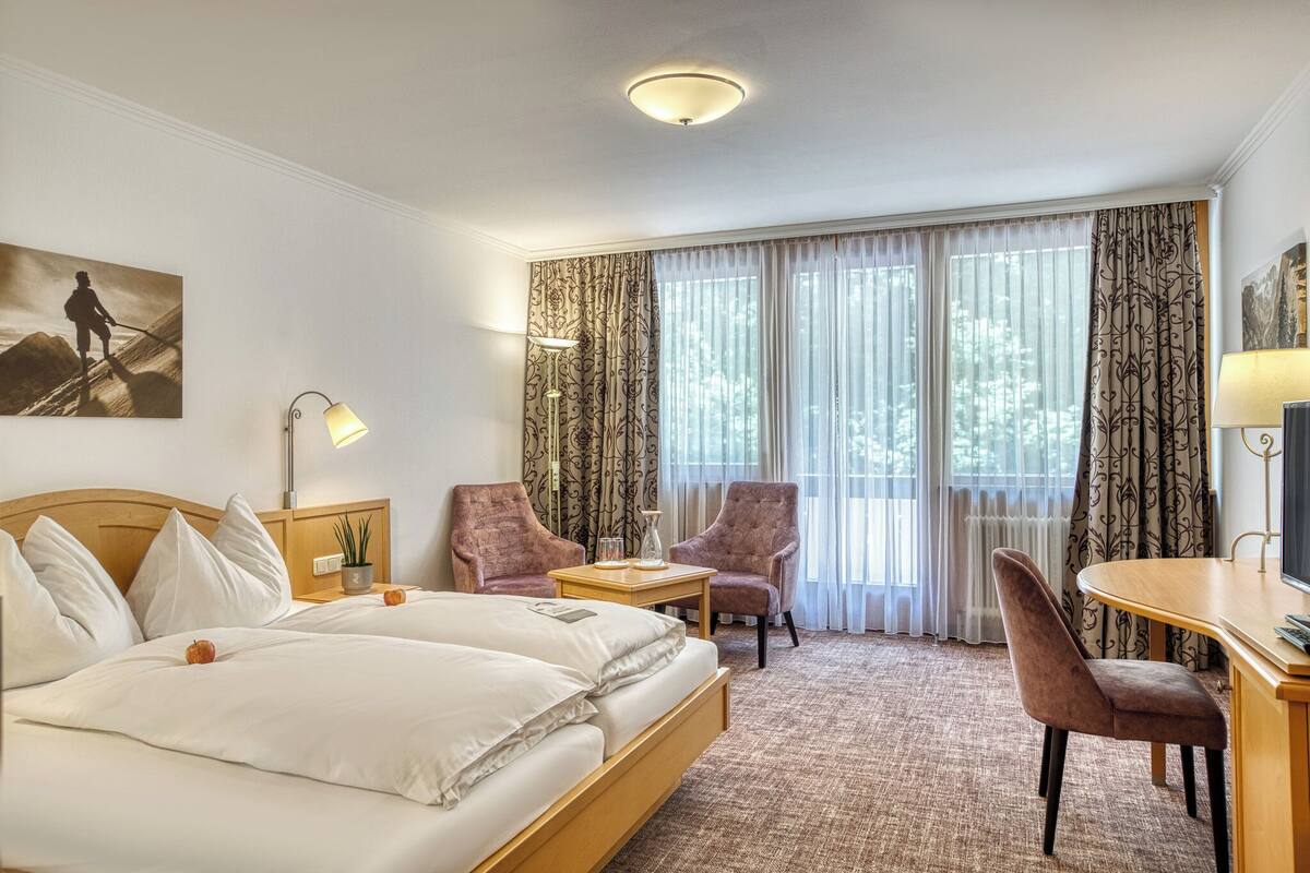 A hotel room with a large bed, two armchairs, a small table, and a desk with a chair.