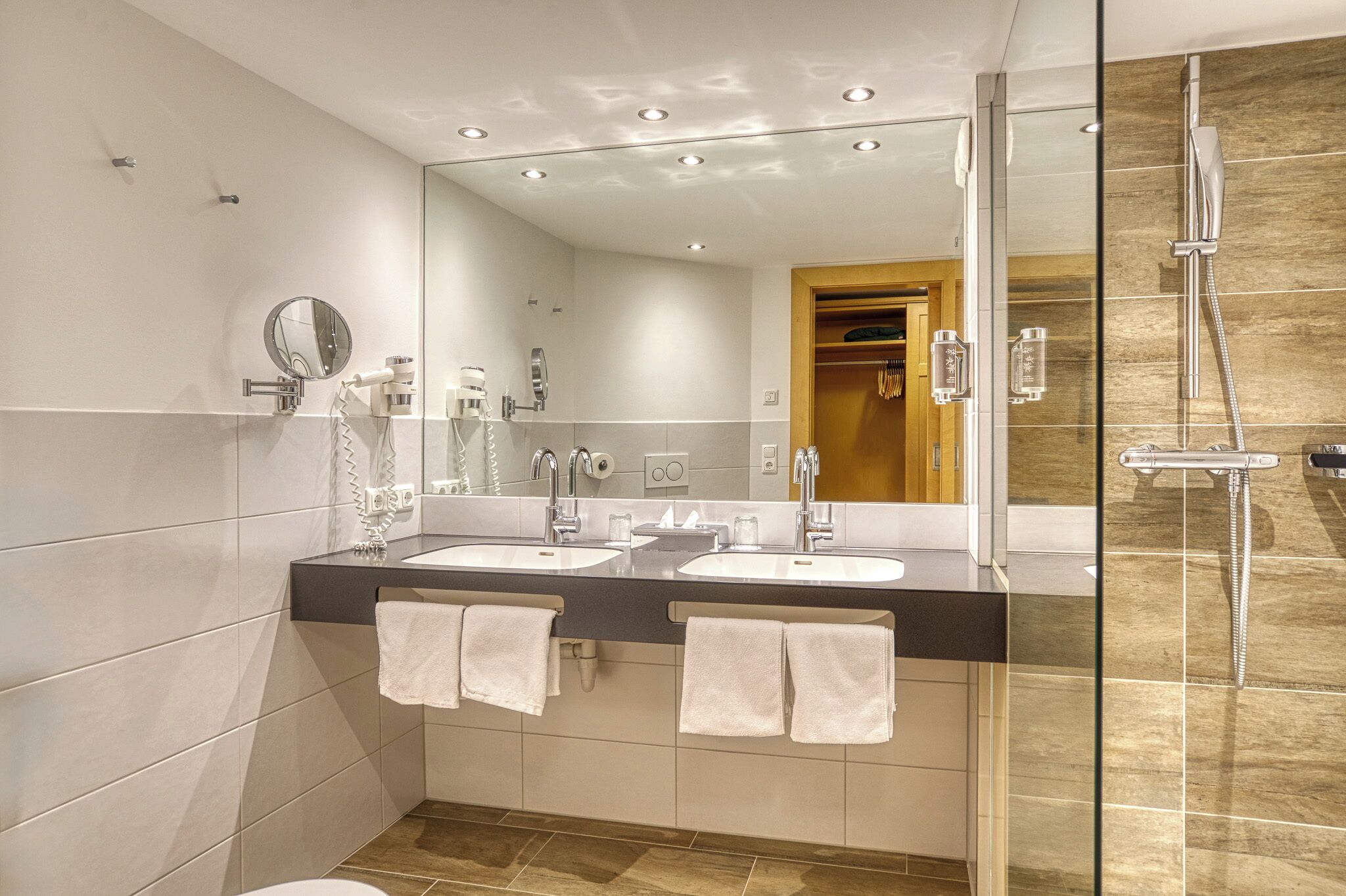 A modern bathroom with two sinks, a large mirror, and a glass-enclosed shower.