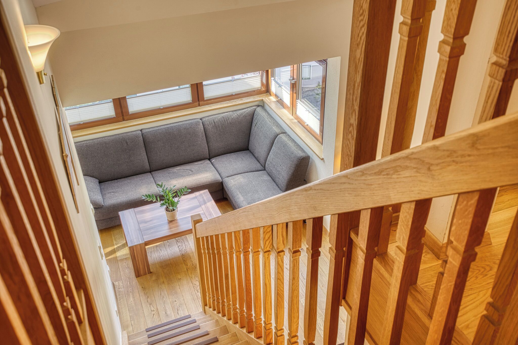 A modern interior with a wooden staircase, a gray sectional sofa, and a small table with a plant.