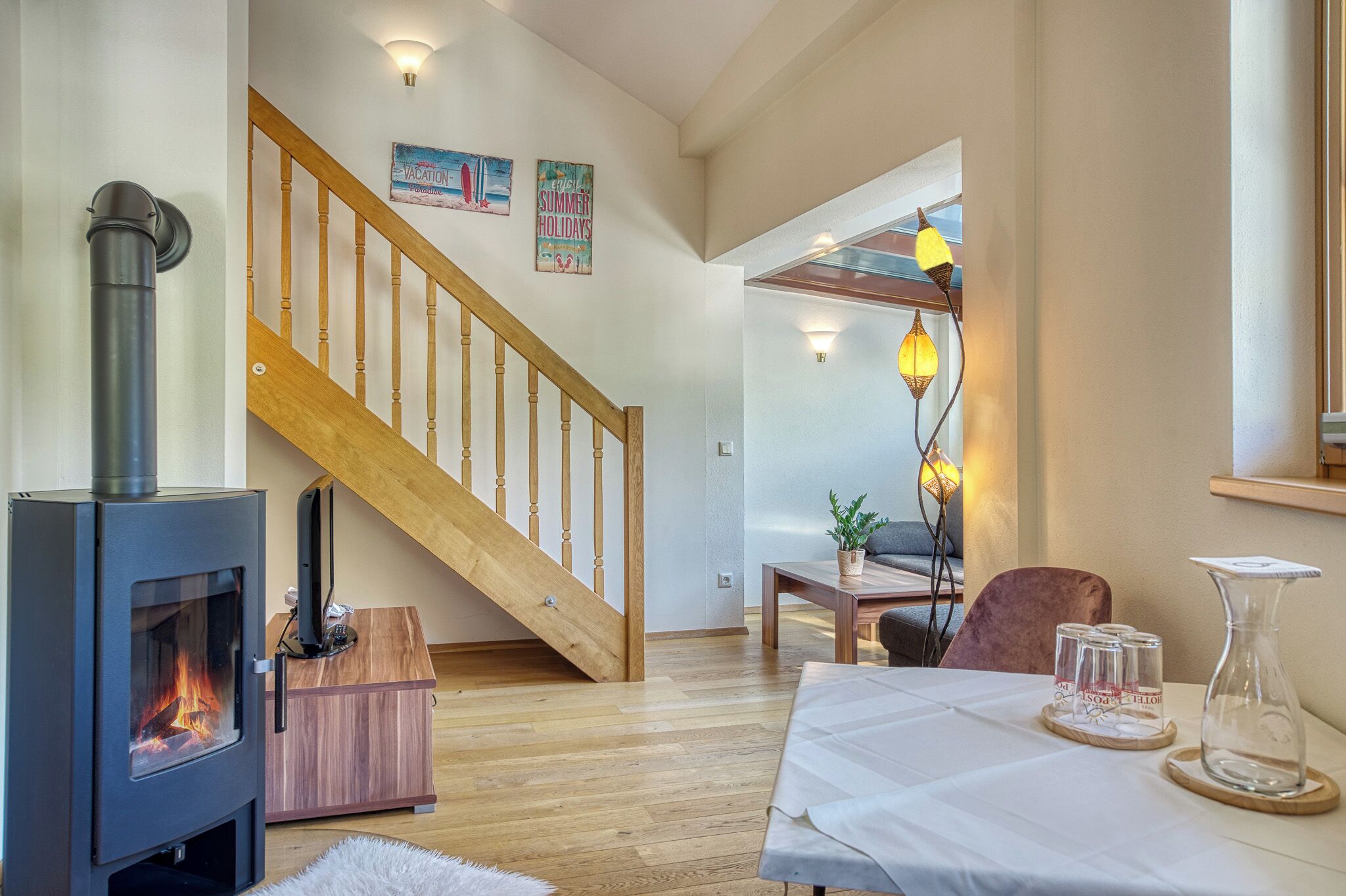 A cozy living room with a wood-burning stove, a wooden staircase, and a dining area with a table set for four.