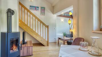 A cozy living room with a wood-burning stove, a wooden staircase, and a dining area with a table set for four.
