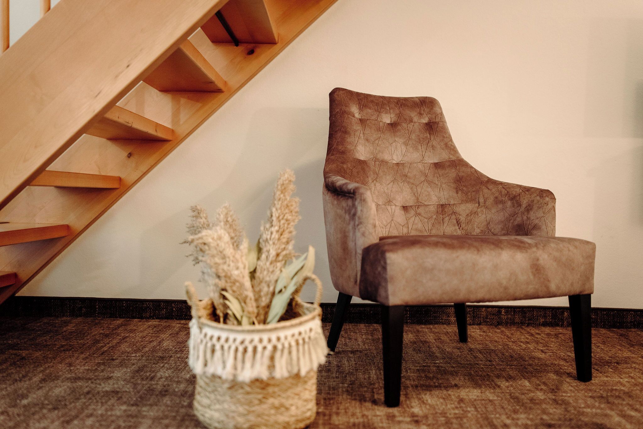 Una silla con tela texturizada, una escalera de madera y una cesta tejida con plantas secas.