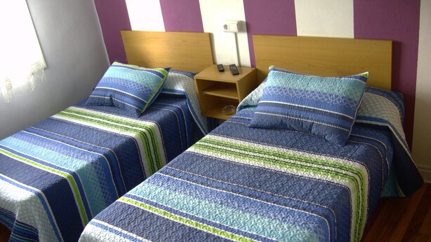 A bedroom with two single beds, each with a blue and green striped bedspread, a wooden headboard, and a nightstand with a lamp. - Pensión Gema Irun (Irun)