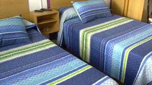 Two single beds with blue and green striped bedding, wooden headboards, and a nightstand with a lamp. - Pensión Gema Irun (Irun)