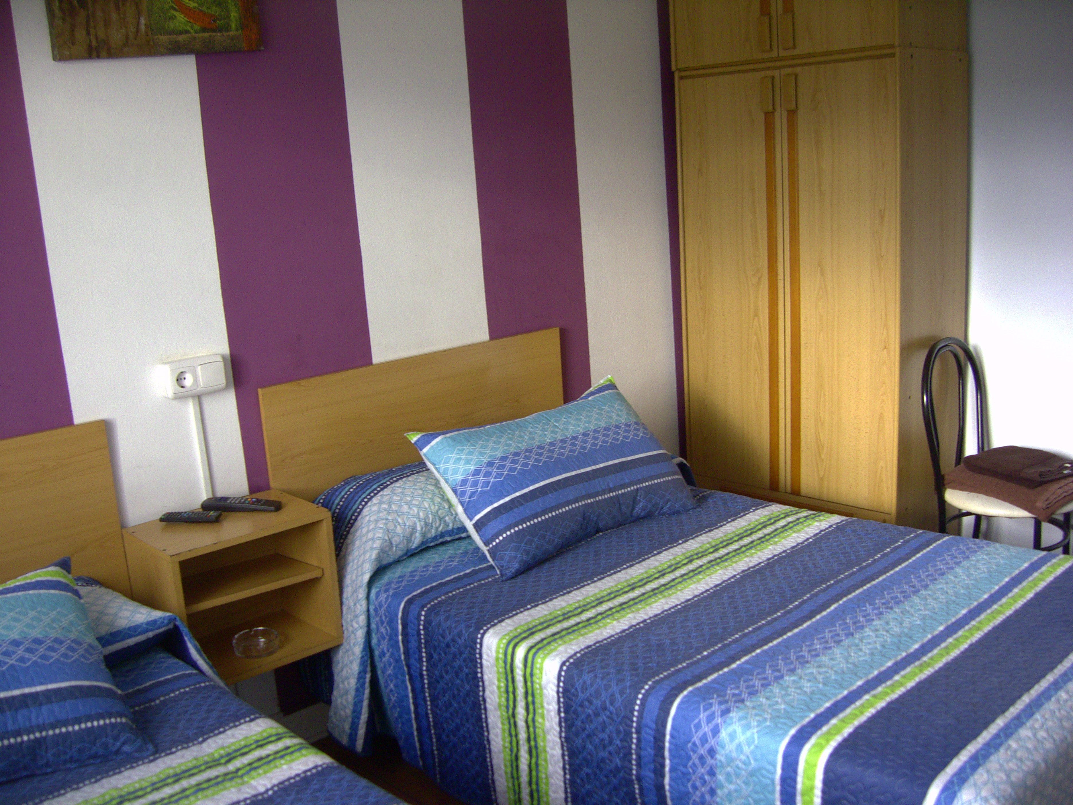 Un dormitorio con dos camas, un armario de madera, una silla y una mesita de noche con lámpara.