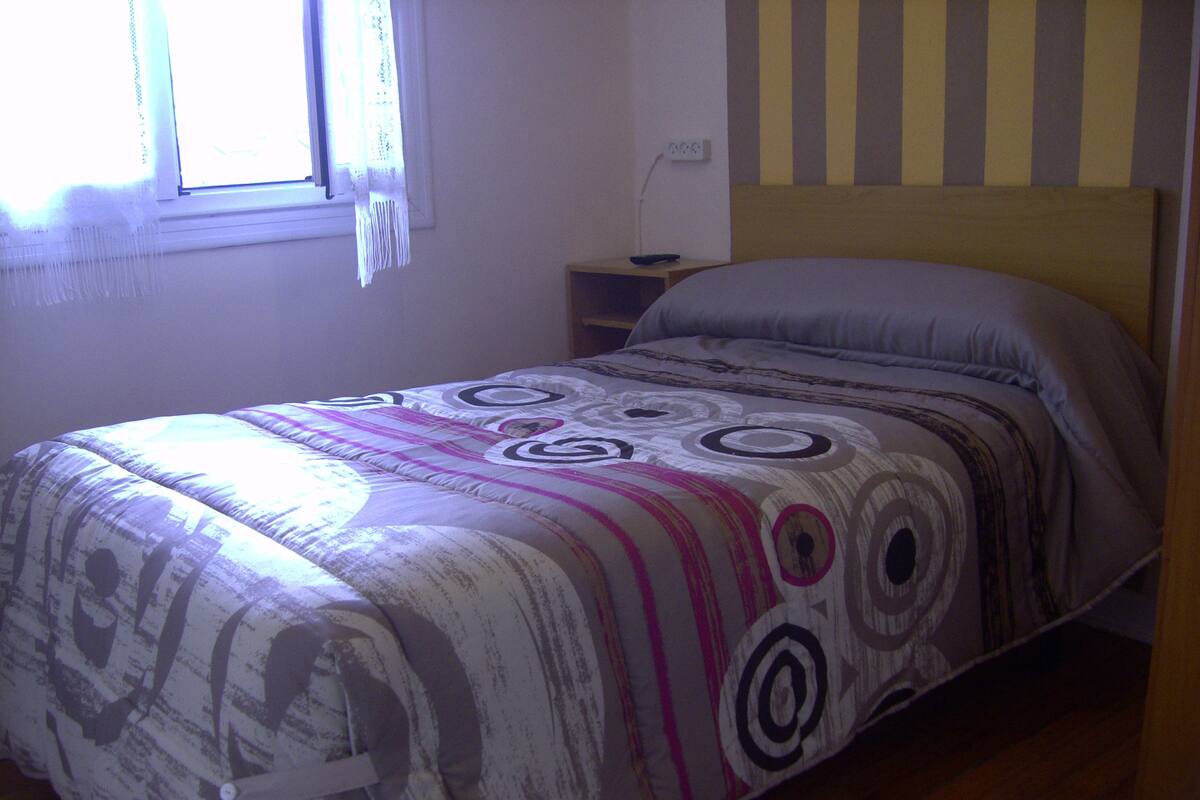 A bedroom with a bed, a nightstand, a lamp, and a window with curtains.